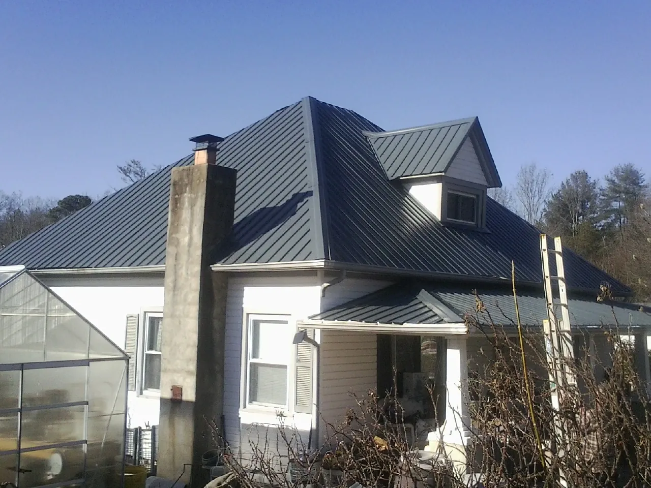 Dark blue standing seam metal roof on a white farmhouse with dormer — Slate & Tile Roof Repair by Roofing Brothers in Swannanoa