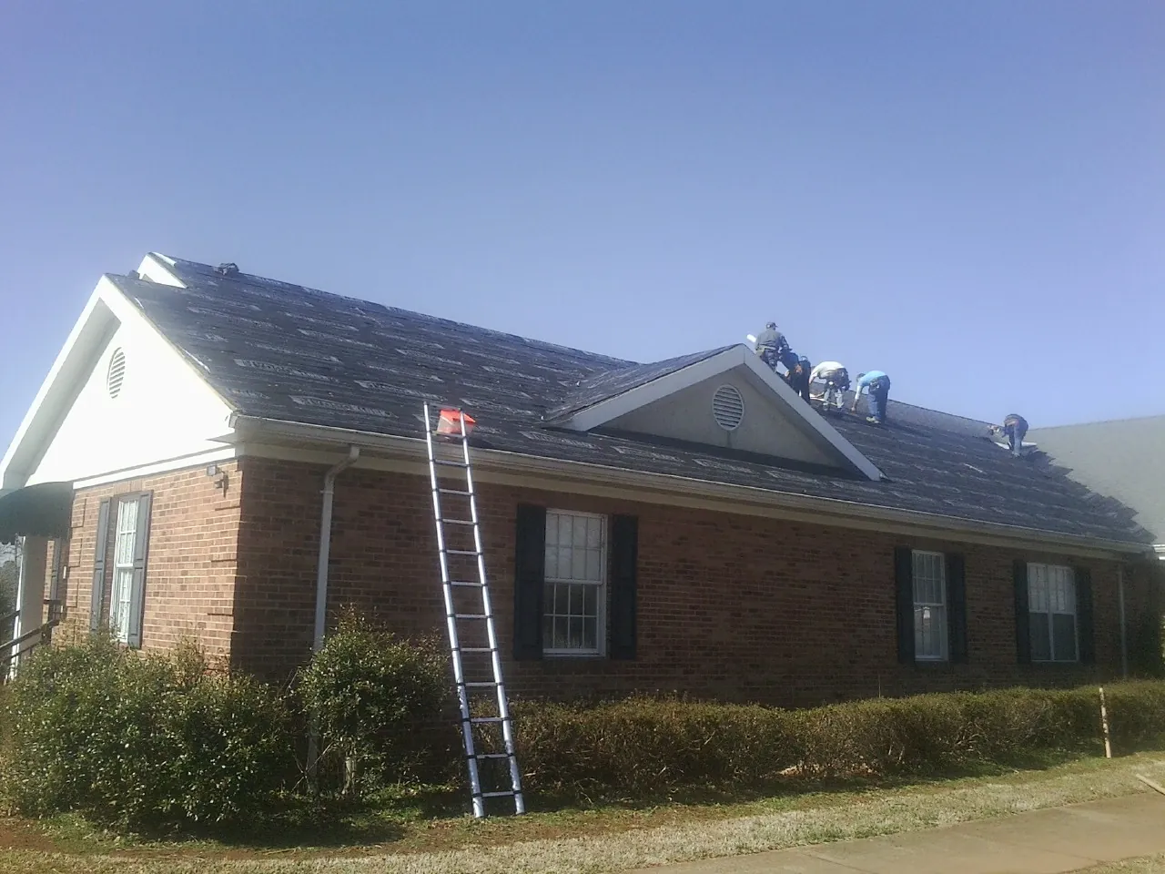Crew tearing shingles off a brick ranch roof with a ladder set — Metal Roof Repair work by our crew in Swannanoa