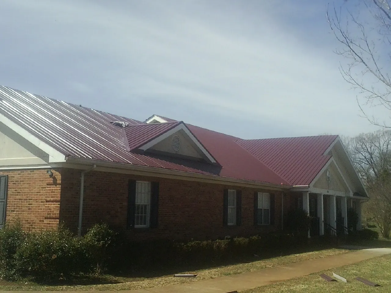 Red metal roof with gabled entries on a long brick building, from a Hail Damage Roof Repair job in Swannanoa