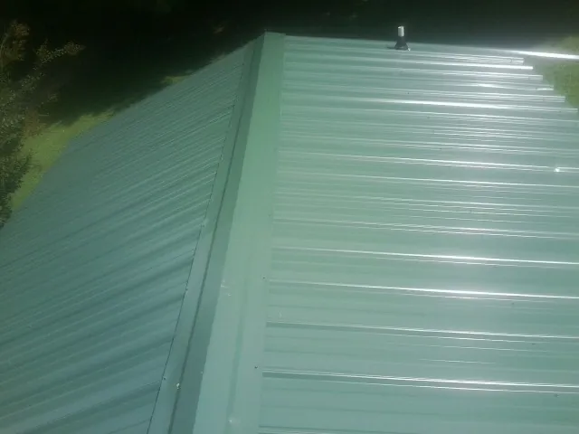 New green metal panels meeting at the ridge of a roof — Flat Roof Repair work by our crew in Swannanoa