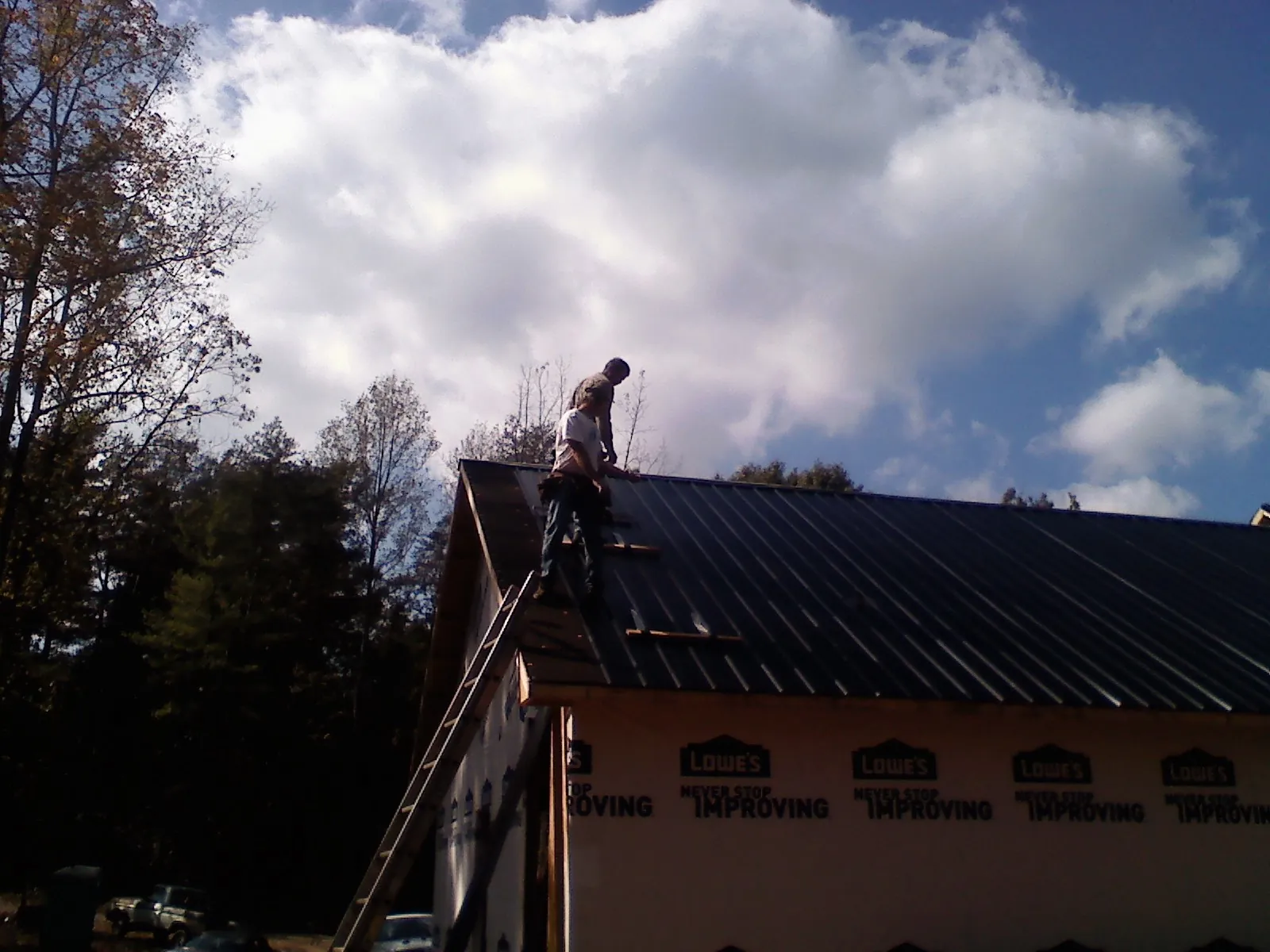 Roofer fastening dark metal panels high against a cloudy sky, from a Roof Inspection job in Swannanoa