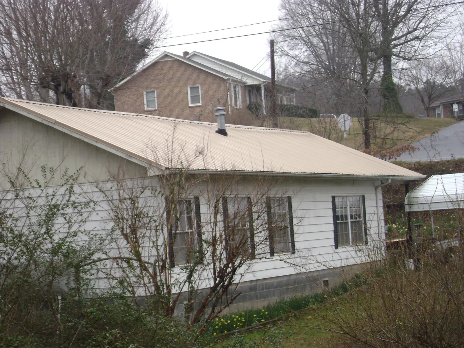 Tan metal roof on a white sided house set into a hillside — Commercial Roofing by Roofing Brothers in Swannanoa