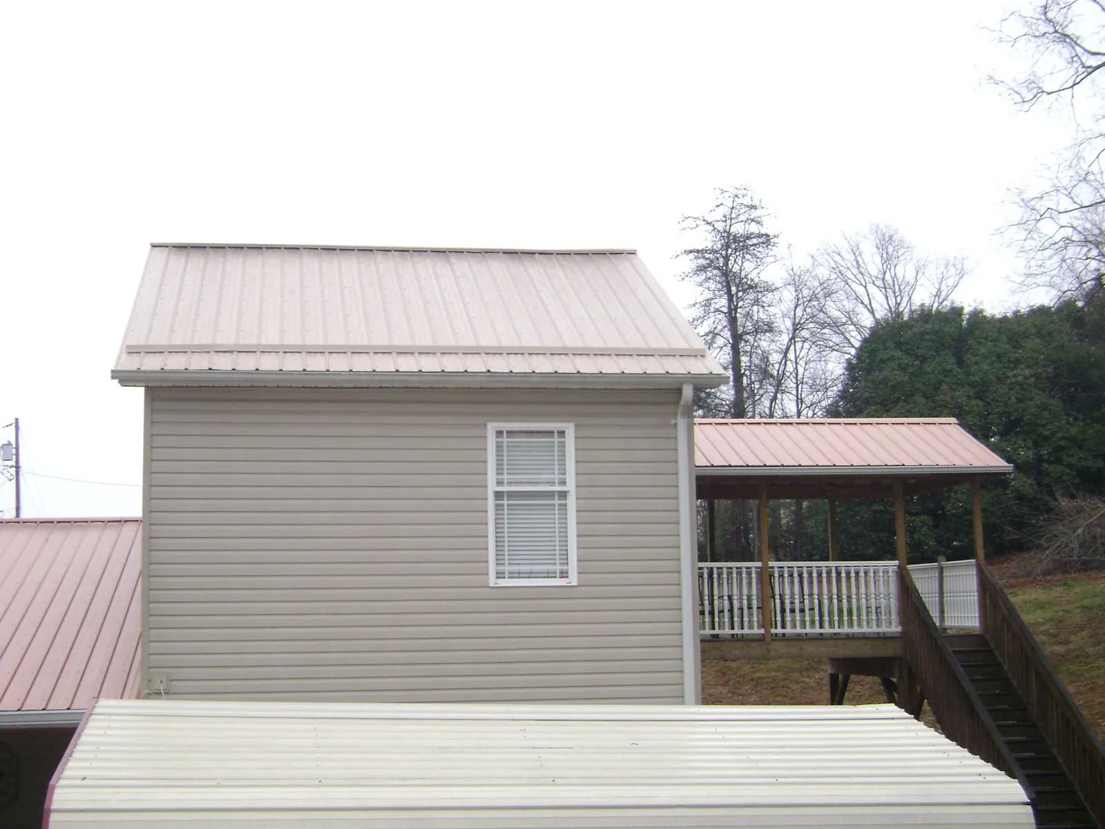 Tan metal roofs on a two story addition and attached porch, from a Roof Replacement job in Swannanoa